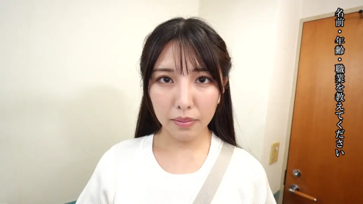 严肃 · 站立 · 面部特写 · 房间 · 注视镜头 · 访谈视角 · 木门 · 白色针织衫