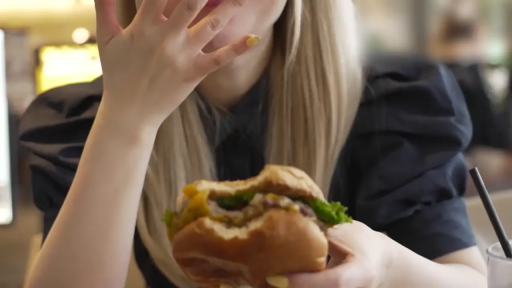 坐姿 · 餐厅 · 金发 · 遮脸 · 汉堡 · 黑色泡泡袖上衣 · 食物与手部特写 · 正在吃汉堡