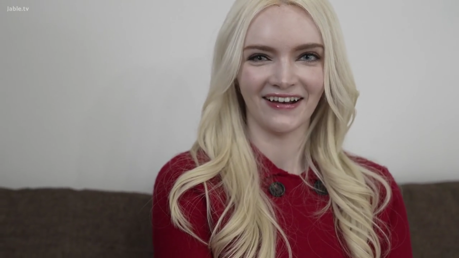 坐姿 · 微笑 · 半身特寫 · 聊天 · 室内沙发 · 红色针织衫 · 长金发